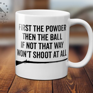 May include: White ceramic coffee mug with a black silhouette of a musket and the text "First the powder then the ball if not that way won't shoot at all".