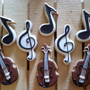May include: A set of nine decorated sugar cookies featuring musical notes and violins. The cookies are decorated with black and white icing and brown icing.