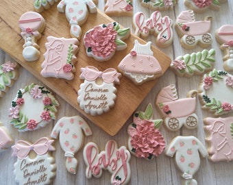 May include: A collection of pink and green baby shower cookies decorated with flowers, baby carriages, and the words "Baby" and "Cameron Danielle Arnett".