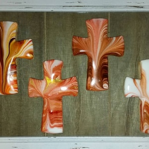 May include: Four wooden crosses with a marbled paint design in shades of orange, brown, and white. The crosses are displayed on a wood panel background.