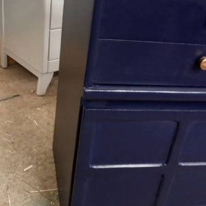 May include: A dark blue dresser with two drawers and a lower cabinet with four doors. The dresser has gold-colored handles.