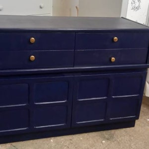 May include: A dark blue wooden cabinet with four drawers and two doors. The cabinet has gold-colored handles.