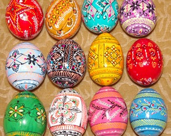 May include: A collection of twelve decorative eggs arranged in a grid, each featuring distinct hand-painted patterns in vibrant colours including red, orange, turquoise, purple, light blue, black, yellow, green, white, and pink with intricate line work.