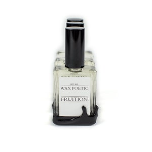 Peut inclure: Quatre flacons en verre transparent avec des bouchons et des &eacute;tiquettes noirs. Les &eacute;tiquettes indiquent "Wax Poetic" et "Fruition". Les flacons sont dispos&eacute;s en rang&eacute;e sur une base noire qui coule.