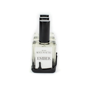 Peut inclure: Un ensemble de quatre flacons en verre transparent avec des bouchons et des &eacute;tiquettes noirs. Les flacons sont dispos&eacute;s en rang&eacute;e et reposent sur une surface noire. Les &eacute;tiquettes indiquent "Wax Poetic" et "Ember".