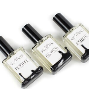 Peut inclure: Trois flacons en verre avec des bouchons noirs et des &eacute;tiquettes indiquant "Wax Poetic" et les noms des parfums : "Flight", "Fruition" et "Ember".