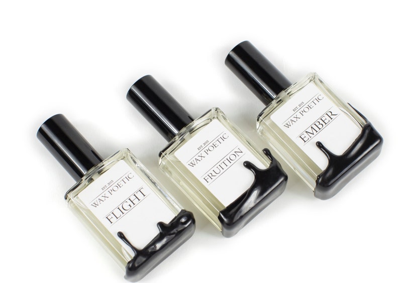 Peut inclure: Trois flacons en verre avec des bouchons noirs et des &eacute;tiquettes indiquant "Wax Poetic" et les noms des parfums : "Flight", "Fruition" et "Ember".