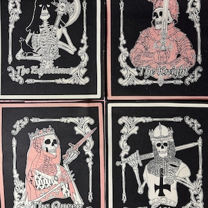 May include: Four black fabric patches with white and pink details. Each patch features a skeleton in a different costume, with the text "The Executioner", "The Knight", "The Queen", and "The King" below each image.