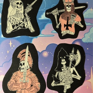 May include: Four iron-on patches featuring skeleton figures in various poses. The skeletons are wearing medieval armour and holding swords and axes. The patches are on a black background with a pink and purple design.