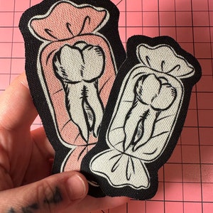 May include: Two iron-on patches featuring a tooth design inside a candy wrapper. One patch has a pink wrapper, and the other has a white wrapper. Both patches have a black border.