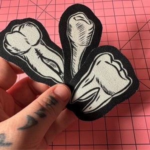 Puede incluir: Tres parches de tela con ilustraciones en blanco y negro de dientes humanos. Cada parche tiene un borde negro y un dibujo detallado estilo grabado de un diente en tinta blanca y negra sobre una base de tela con textura visible.