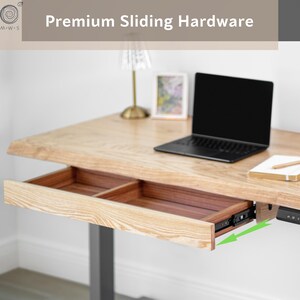 May include: A light-colored wooden desk with an open drawer, a laptop, and a small lamp. The drawer is open, revealing a dark brown interior. The desk has a modern design with a gray metal base. The text "Premium Sliding Hardware" is at the top.