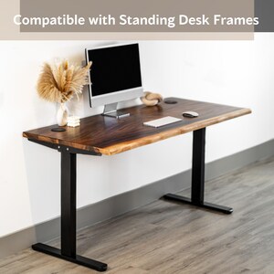 May include: A solid wood standing desk top replacement with a black metal frame. The desk top has a live edge and is compatible with standing desk frames. A computer monitor, keyboard, and mouse are on the desk.