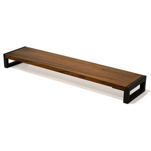 May include: A long, rectangular wooden monitor stand with black metal brackets. The shelf is made of dark wood and has a natural finish. The brackets are simple and modern in design.
