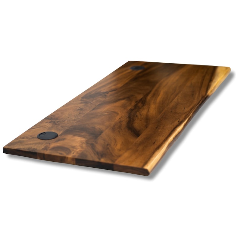 May include: A long, rectangular walnut desk top with a natural walnut finish. The desk top has a slightly curved live edge and two black grommets for cable management.