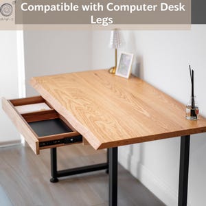 May include: Wooden desk with a natural wood grain finish. The desk has a drawer that is partially open, revealing a black interior. The desk is supported by black metal legs. The text "Compatible with Computer Desk Legs" is at the top.