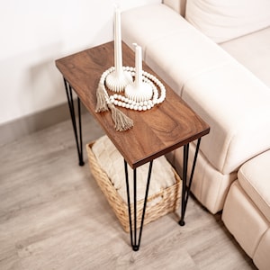 May include: A wooden side table with black hairpin legs. The end table has a white beaded garland and two white candles on top. The wood side table is sitting on a white rug.