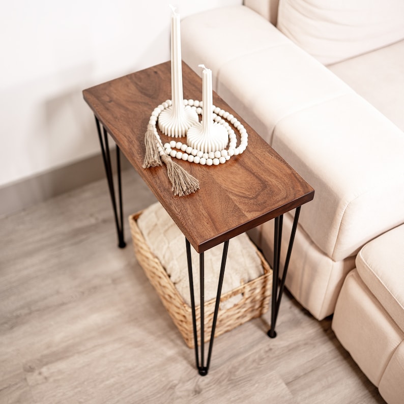 May include: A wooden side table with black hairpin legs. The end table has a white beaded garland and two white candles on top. The wood side table is sitting on a white rug.