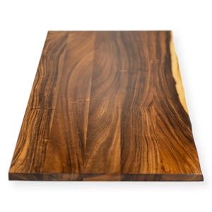 May include: A rectangular wooden cutting board with a natural edge. The board is made of dark brown wood with a prominent grain pattern. The wood has a smooth, polished finish, and the edges are slightly rounded.