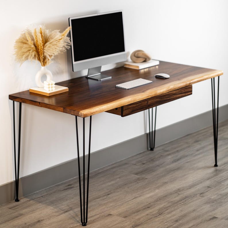May include: A dark solid wood desk with a single drawer and hairpin legs. The desk has a live edge and is topped with a computer monitor, keyboard, and mouse.