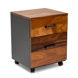 May include: A two-drawer mobile file cabinet with a black base and a wood top. The drawers have walnut wooden fronts with dark brown metal handles.