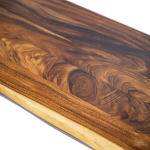 May include: Close-up of a solid-wood desktop with a rich walnut color and a natural wood-grain pattern. The tabletop has a smooth, polished surface and a slightly rounded edge.