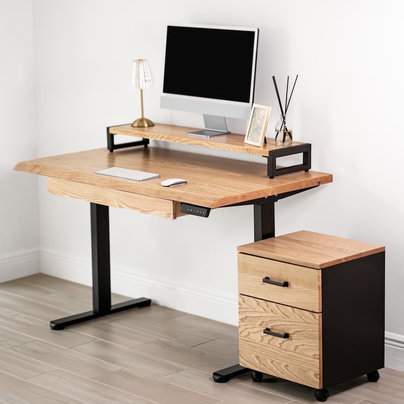 May include: A white oak standing desk with drawer and a matching two-drawer cabinet. The desk has a monitor stand. A computer monitor, lamp, and accessories are on the desk.