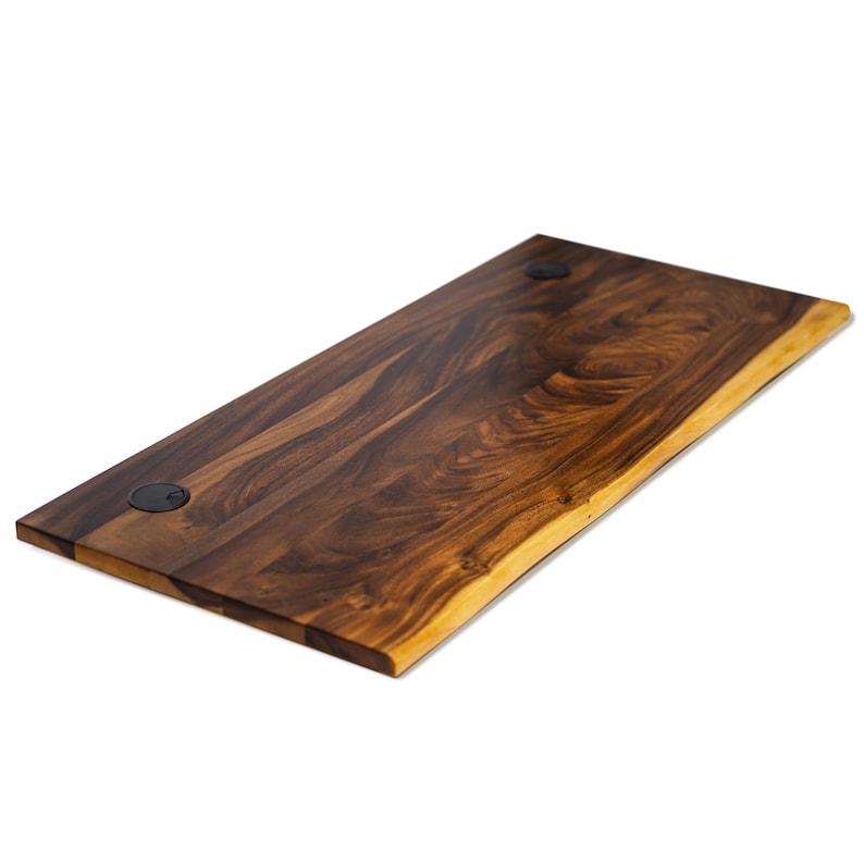 May include: A rectangular walnut desk top with a live edge. The tabletop is made of dark brown wood with a natural grain pattern and two black metal accents. The edge is a lighter, golden brown color.