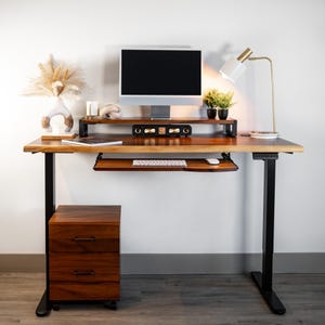 May include: Solid walnut standing desk with black height-adjustable legs, keyboard tray, monitor stand, and rolling file cabinet in a modern home office workspace.
