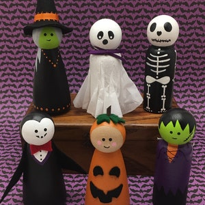 May include: Set of six Halloween-themed wooden peg dolls. The dolls are painted in various colors and designs, including a witch, a ghost, a skeleton, a vampire, a pumpkin, and a Frankenstein's monster.