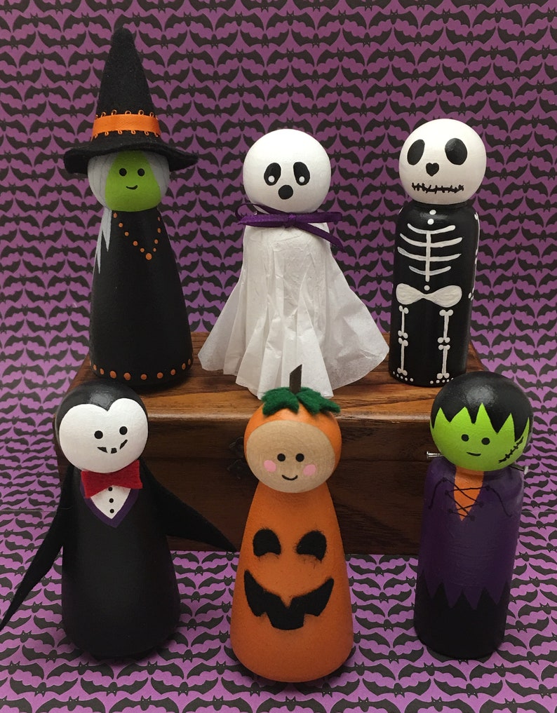 May include: Set of six Halloween-themed wooden peg dolls. The dolls are painted in various colors and designs, including a witch, a ghost, a skeleton, a vampire, a pumpkin, and a Frankenstein's monster.