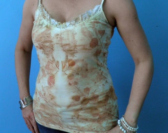 May include: A woman wearing a light brown tank top with a floral pattern and a silver chain necklace. She is wearing a silver bracelet on her left wrist and a pearl bracelet on her right wrist. She is standing in front of a blue wall.