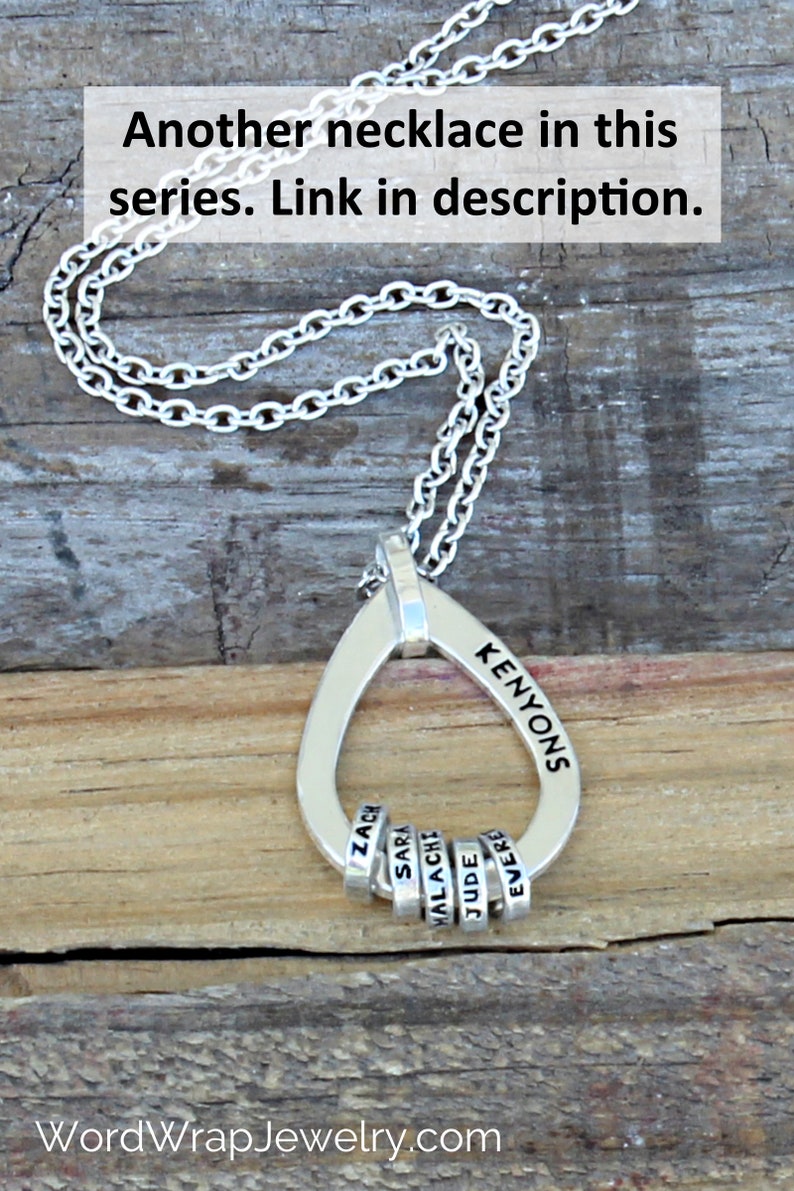 May include: Silver pendant necklace with a teardrop-shaped pendant and chain. The pendant is engraved with the name "KENYONS" and has small rings with names. The image includes the text "Another necklace in this series. Link in description."