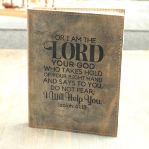 May include: A brown leather-bound book with the text "FOR I AM THE LORD YOUR GOD WHO TAKES HOLD OF YOUR RIGHT HAND AND SAYS TO YOU, DO NOT FEAR; I Will Help You. Isaiah 41:13" in black lettering. The book is standing upright.