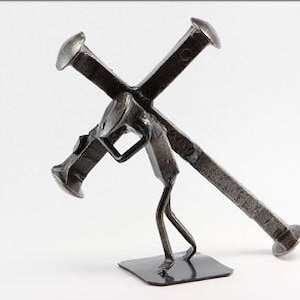 以下が含まれることがあります： 釘でできた十字架を運ぶ人の金属彫刻。彫刻はリサイクルされた金属で作られており、素朴な仕上がりです。