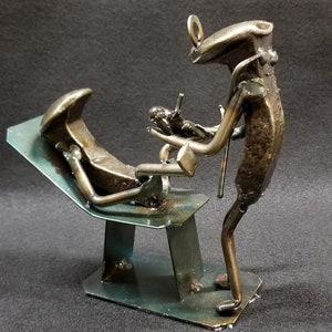 Puede incluir: Una escultura de metal de un dentista examinando a un paciente en una silla dental. La escultura está hecha de metal reciclado y está pintada con un acabado metálico.