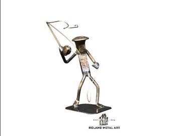 May include: A metal sculpture of a person fishing. The sculpture is made of nails and wire. The person is holding a fishing rod and has a fish on the line. The sculpture is on a wooden base. The sculpture is signed "Roland Metal Art".