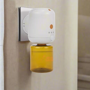 Può includere: Un diffusore di oli essenziali bianco e arancione collegato a una presa a muro. Il diffusore ha un design cilindrico con un serbatoio di olio trasparente color ambra. Il dispositivo è dotato di un pulsante arancione e tre spie.