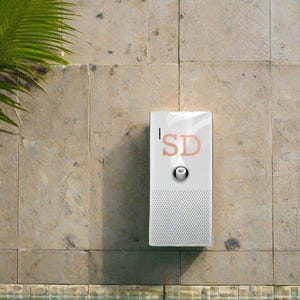 May include: White speaker with a black speaker grille and a small white button. The speaker has the text "SD" in orange letters on the front. The speaker is mounted on a tiled wall next to a swimming pool.