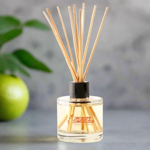 May include: A clear glass bottle with a black lid and wooden sticks, filled with a light yellow liquid. The bottle has a label that reads "Sensory Decisions Unique Fragrances".