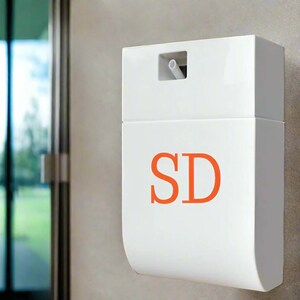 Op de afbeelding: Witte, wandgemonteerde dispenser met een doorzichtige plastic spuitmond en de letters "SD" in oranje.