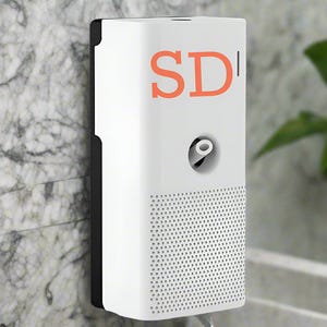 Op de afbeelding: Een wit rechthoekig apparaat met de oranje letters "SD" op de voorkant. Het apparaat heeft een geperforeerd onderste gedeelte en een zwarte rand aan de linkerkant. Het is gemonteerd op een muur met marmerpatroon.