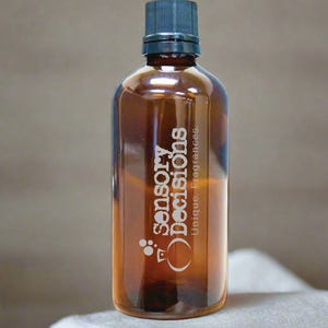 Puede incluir: Una botella de vidrio marrón con una tapa negra y el texto "sensory decisions unique fragrances" grabado en el lateral.