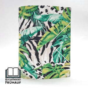 Könnte beinhalten: Ein Notizbuch mit Stoffbezug, der ein tropisches Blatt- und Zebrastreifenmuster aufweist. Der Einband zeigt eine Mischung aus Grün, Gelb und Weiß mit einem weißen Gummibandverschluss. Der Text "BUCHBINDEREI FRÜHAUF" ist unten links aufgedruckt.