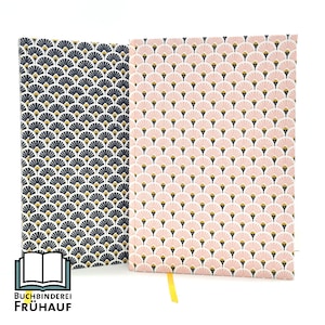 Pode incluir: Dois cadernos com um padrão geométrico de leques rosa e dourados sobre um fundo branco. O caderno à esquerda tem um fundo azul marinho e o caderno à direita tem um fundo rosa claro.