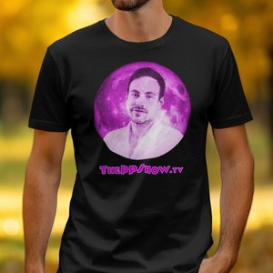 Puede incluir: Camiseta negra con un gráfico morado de la cara de un hombre en un círculo con un fondo de galaxia. El texto "THEPPSHOW.TV" está impreso en morado debajo del gráfico.