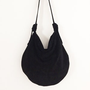 May include: A black, round, fabric tote bag with a long strap. The bag is made of a soft, textured fabric and has a gathered, slouchy look.