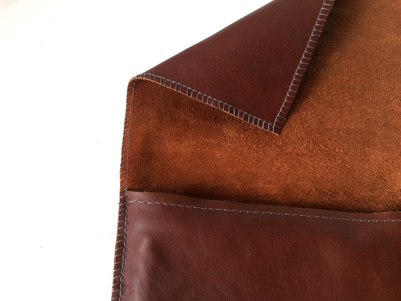 May include: A brown leather pouch with a suede lining. The pouch is closed with a flap and has a stitched edge.