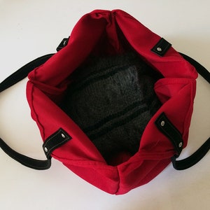 May include: Red tote bag with black straps and silver accents. The bag is open and empty, showing the black fabric lining.