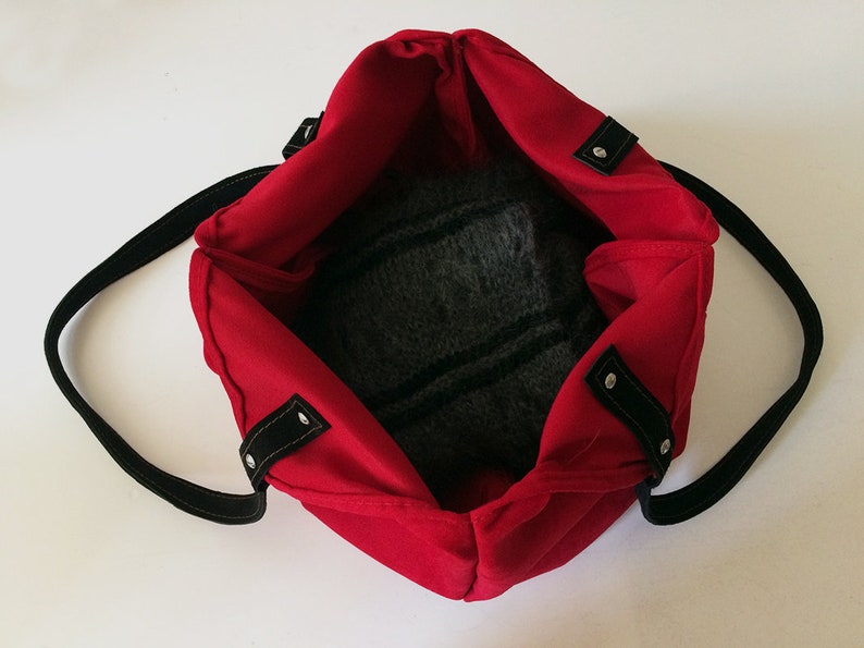 May include: Red tote bag with black straps and silver accents. The bag is open and empty, showing the black fabric lining.